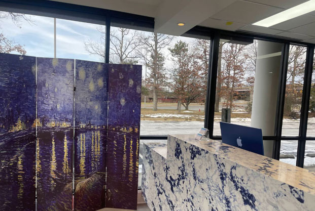 The image shows an indoor setting with a large painting hanging on a wall displaying a night scene with a bridge and city lights, placed next to a window with a view of a snowy landscape under a clear sky.