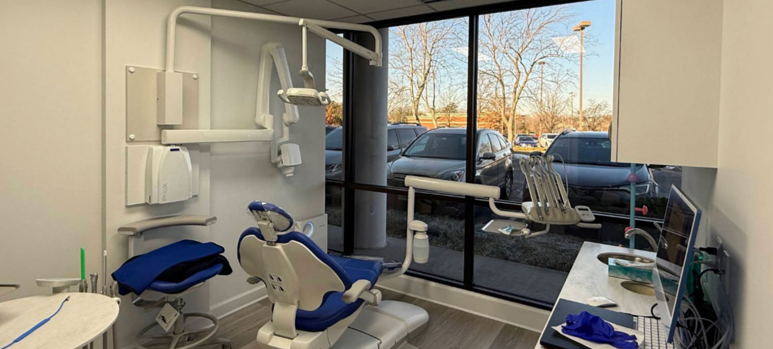 The image shows an interior view of a dental office with dental chairs, equipment, and a window allowing natural light into the space.