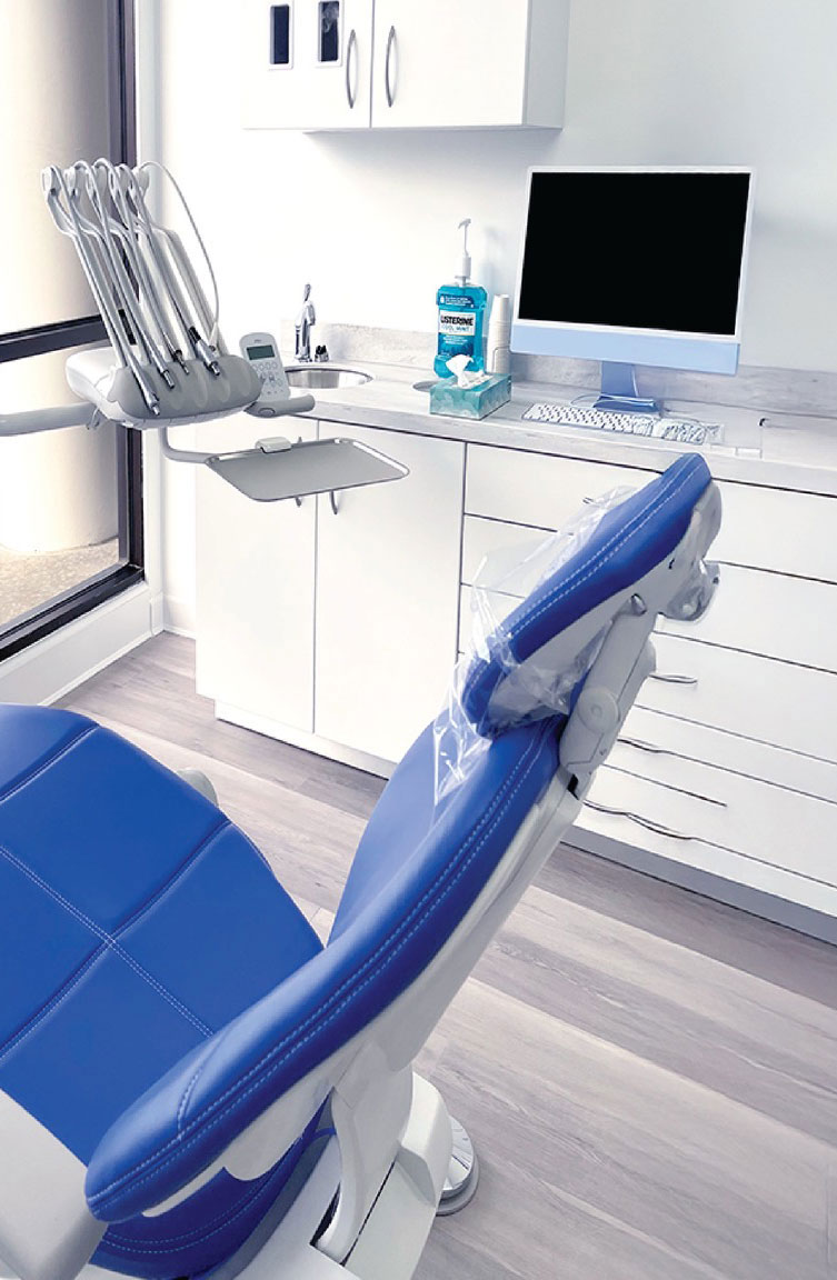 The image shows a modern dental office interior with a dental chair and equipment, a computer desk with a monitor, keyboard, and mouse, and a window revealing an outdoor view.