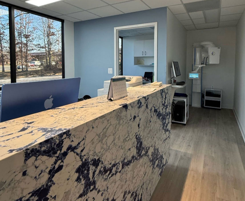 The image shows an office interior with a marble countertop, a desk with a computer monitor, and a reception area with a window view of trees.