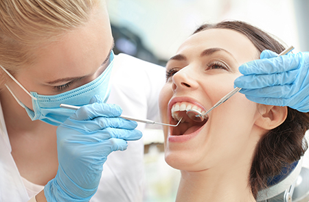 A dental hygienist in protective gear is cleaning a patient s teeth during a dental appointment.