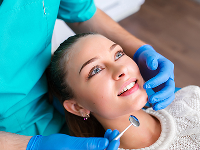 The image shows a dental professional performing a procedure on a patient's teeth, with the patient smiling and looking at the camera.